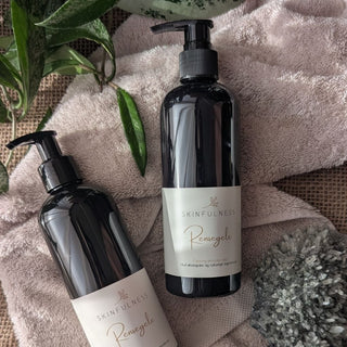 Rensegele in a black pump bottle, placed on a soft towel with greenery and a textured stone nearby.