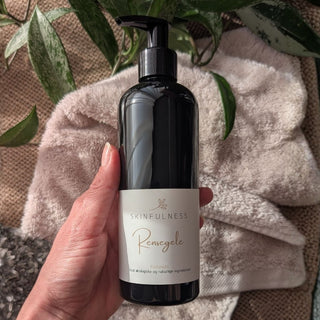 Rensegele in a black pump bottle held by a hand, with a soft towel and green plants in the background.